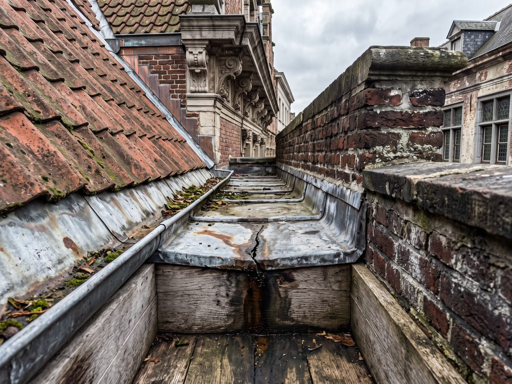 Ingewerkte bakgoot achter de kroonlijst van een oudere woning, met zinken bekleding en een gescheurde naad