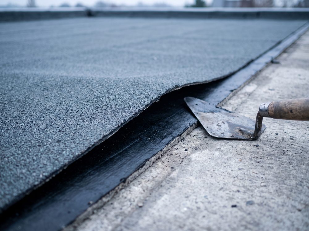 Doorsnede van een tweelaagse bitumenopbouw op een plat dak, met de onderlaag en de toplaag met leislag zichtbaar